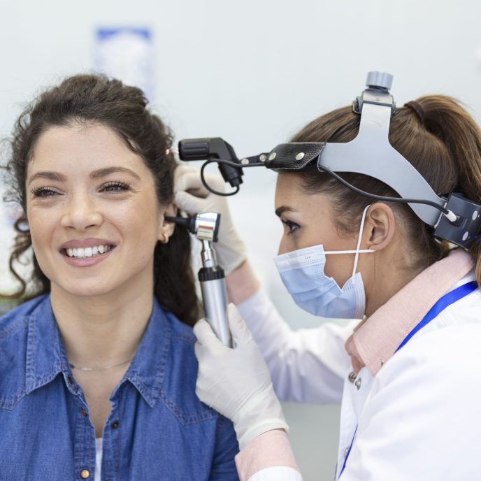 Hearing exam. Otolaryngologist doctor checking woman's ear using otoscope or auriscope at medical clinic.