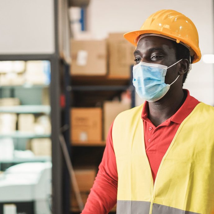 African warehouse man working while wearing safety mask - Focus on face